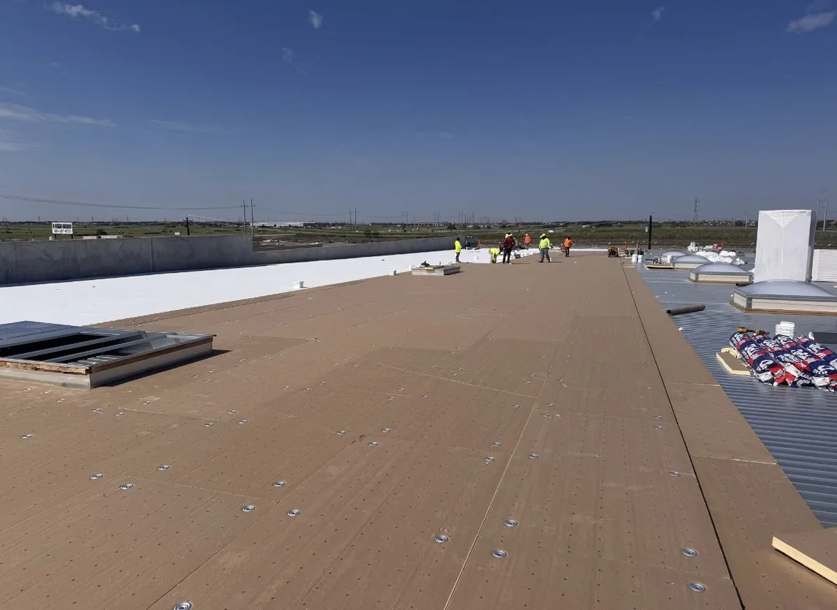 Crew fastening cover board over a metal deck before installing a white single-ply roof